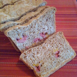A loaf of mango and raspberry wheat bread, cut into slices on a red background