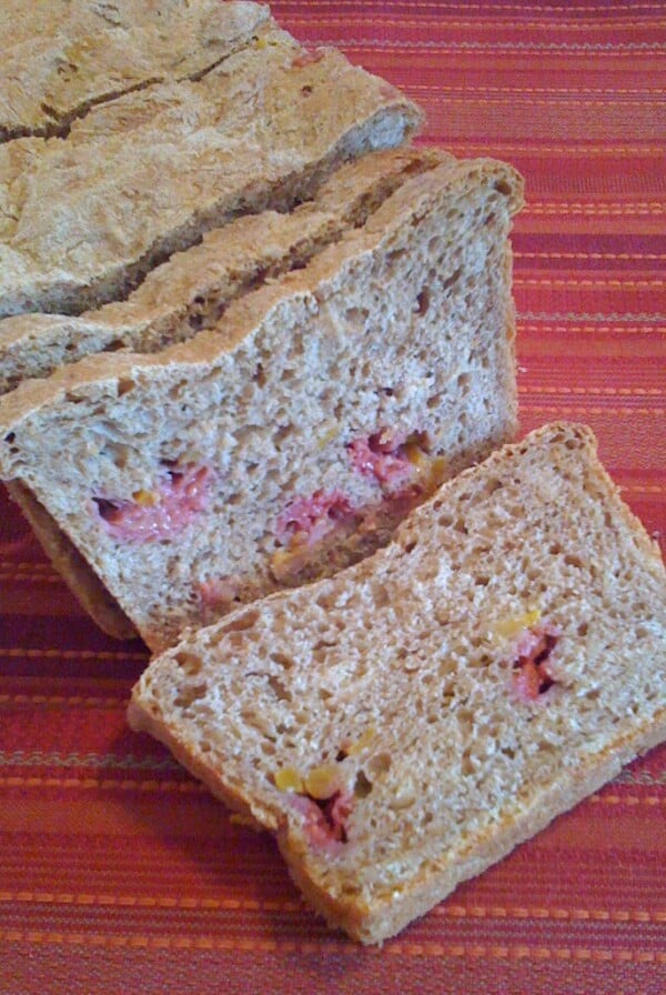 A loaf of mango and raspberry wheat bread, cut into slices on a red background