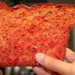 A slice of beetroot bread with orange zest being held up towards the camera