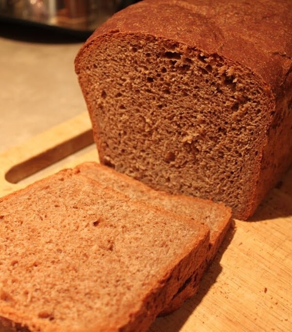 A loaf of chocolate bread with the end sliced off, on a wooden chopping board