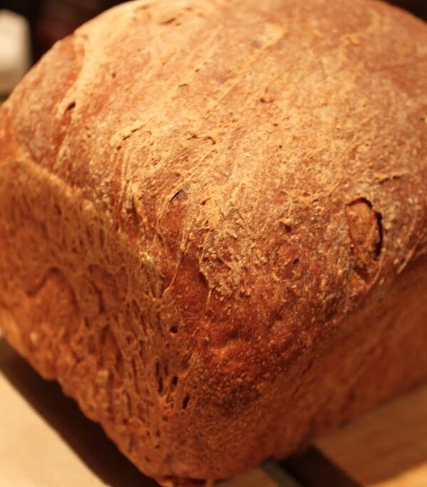 A loaf of Blueberry Apple Wheat Bread on a wooden chopping board