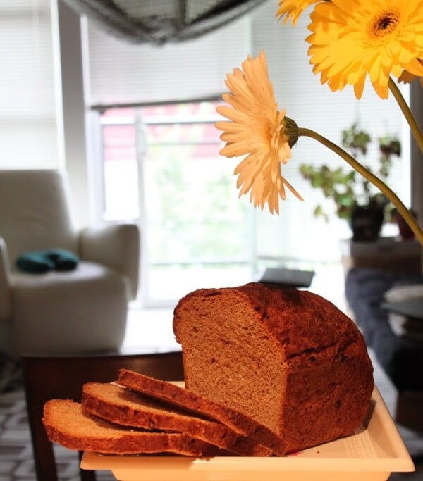 A loaf of date maple wheat bread cut into slices next to a bunch of flowers