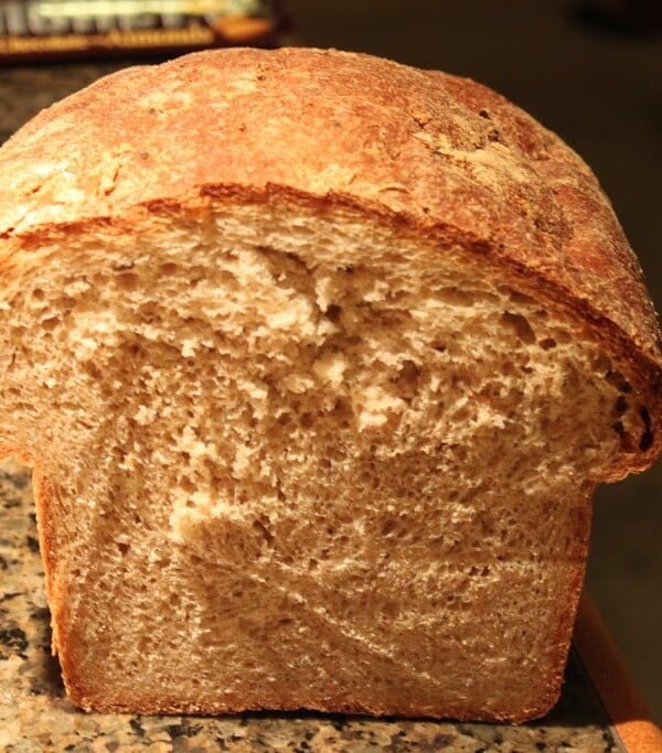 A loaf of wheat oat flax bread cut in half on a work surface