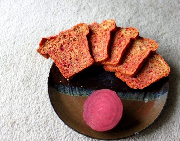 Slices of beet and blueberry mini loaf arranged on a plate with a slice of beet