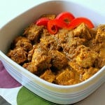 A spinach tomato curry in a white bowl with red pepper garnish