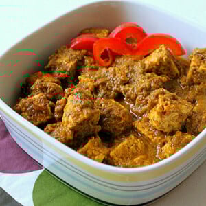 A spinach tomato curry in a white bowl with red pepper garnish
