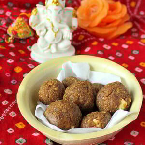 Besan laddoo in a pale bowl on a red background