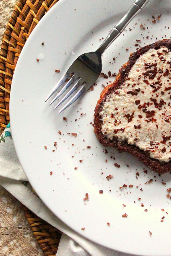 A slice of French toast on a white plate with a fork. Sprinkled with cocoa powder