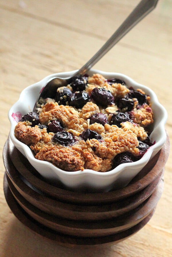 A ramakin on a woooden work surface with Baked French Toast in it. A spoon sticking out of the crisp