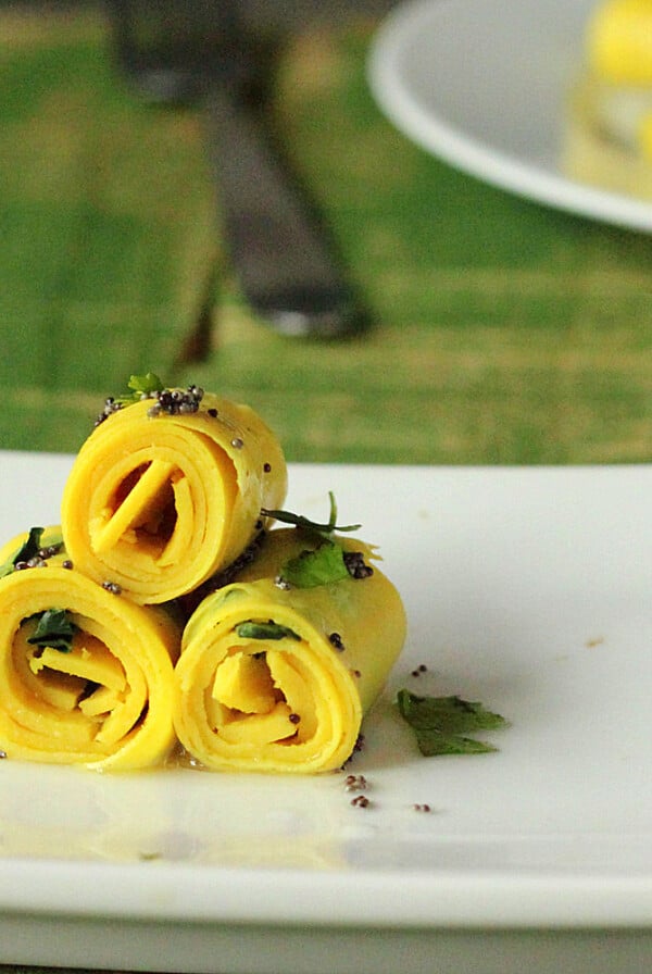 Three khandvi rolled up on a white plate and sprinkled with herbs