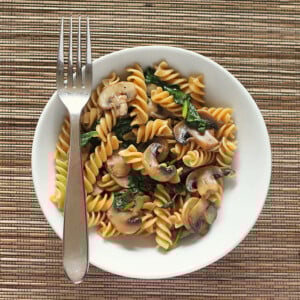 Mushroom fusilli in a white bowl with a fork. On a bamboo mat