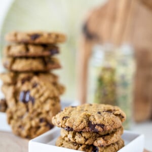 pistachio cookies on white plate with stack of vegan cookies in bakground on wooden board