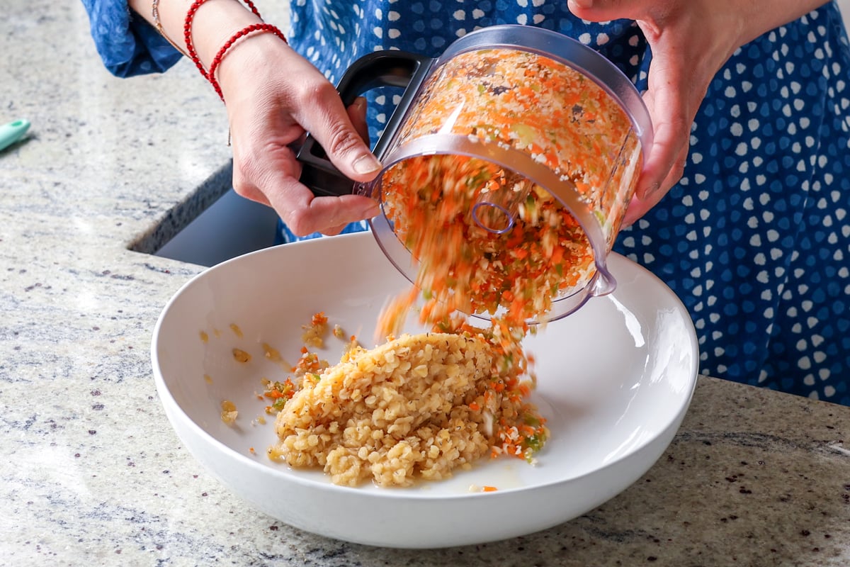 adding chopped veggies from the food processor to a bowl of cooked red lentils