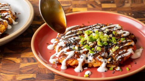 spooning the tonkatsu sauce onto the okonomiyaki