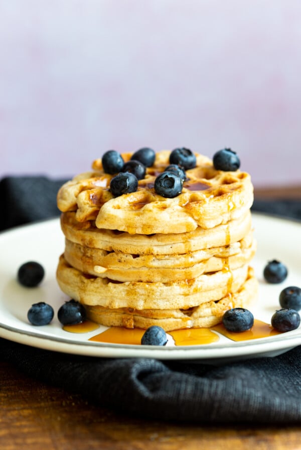 Our Easy Vegan Waffles stacked on a white plate over black napkin