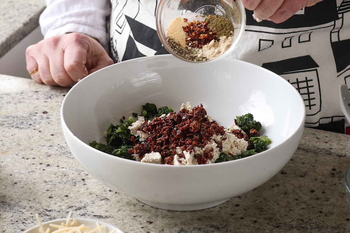 adding sun-dried tomato and spices to the bowl of spinach