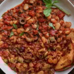 close-up of puttanesca beans on a plate with garlic bread