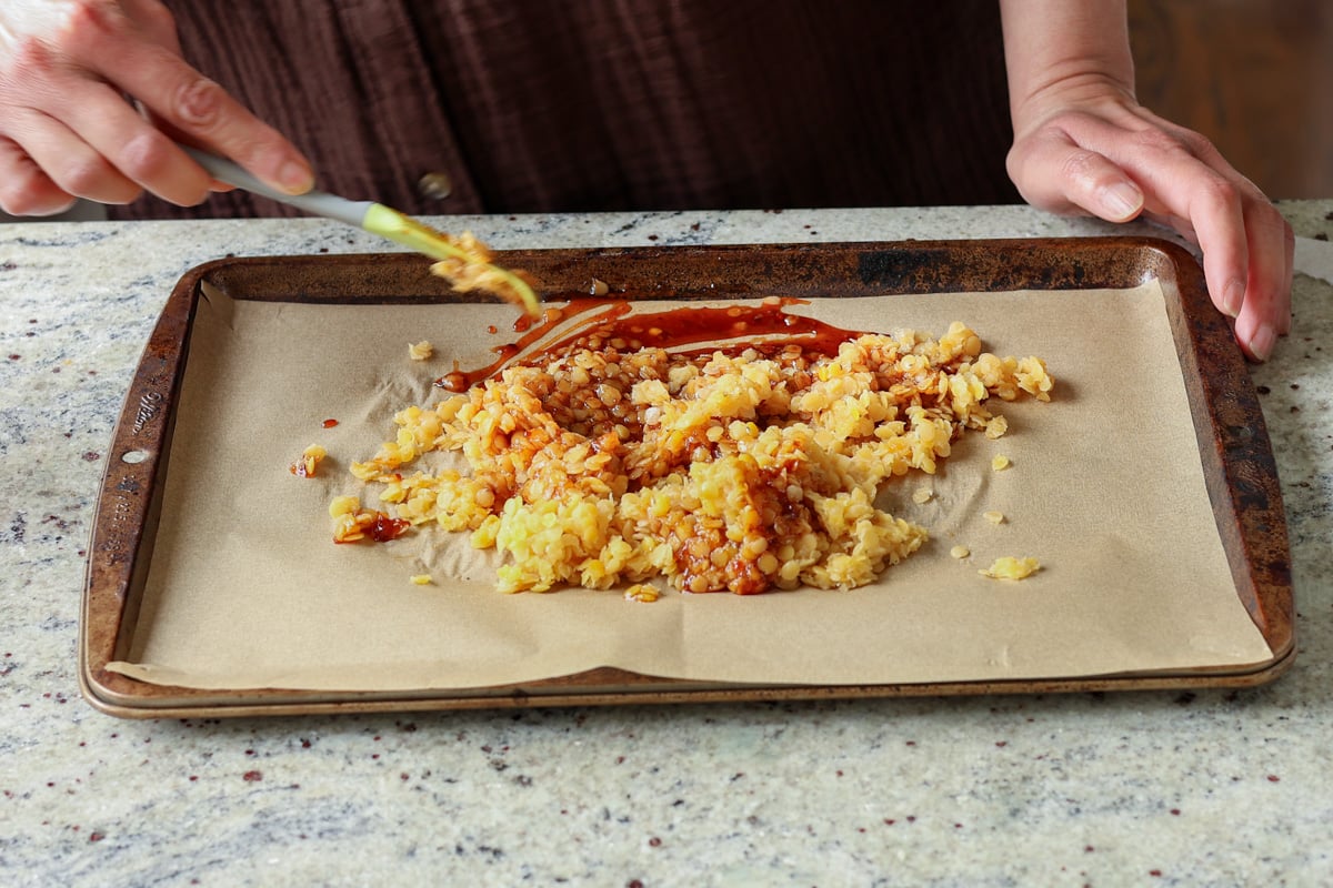 spreading the peanut gochujang savory lentil granola mixture onto the baking pan