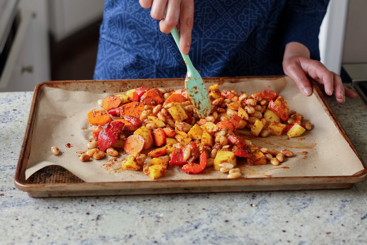 tossing the beans and veggies in the spice mixture on the sheet pan