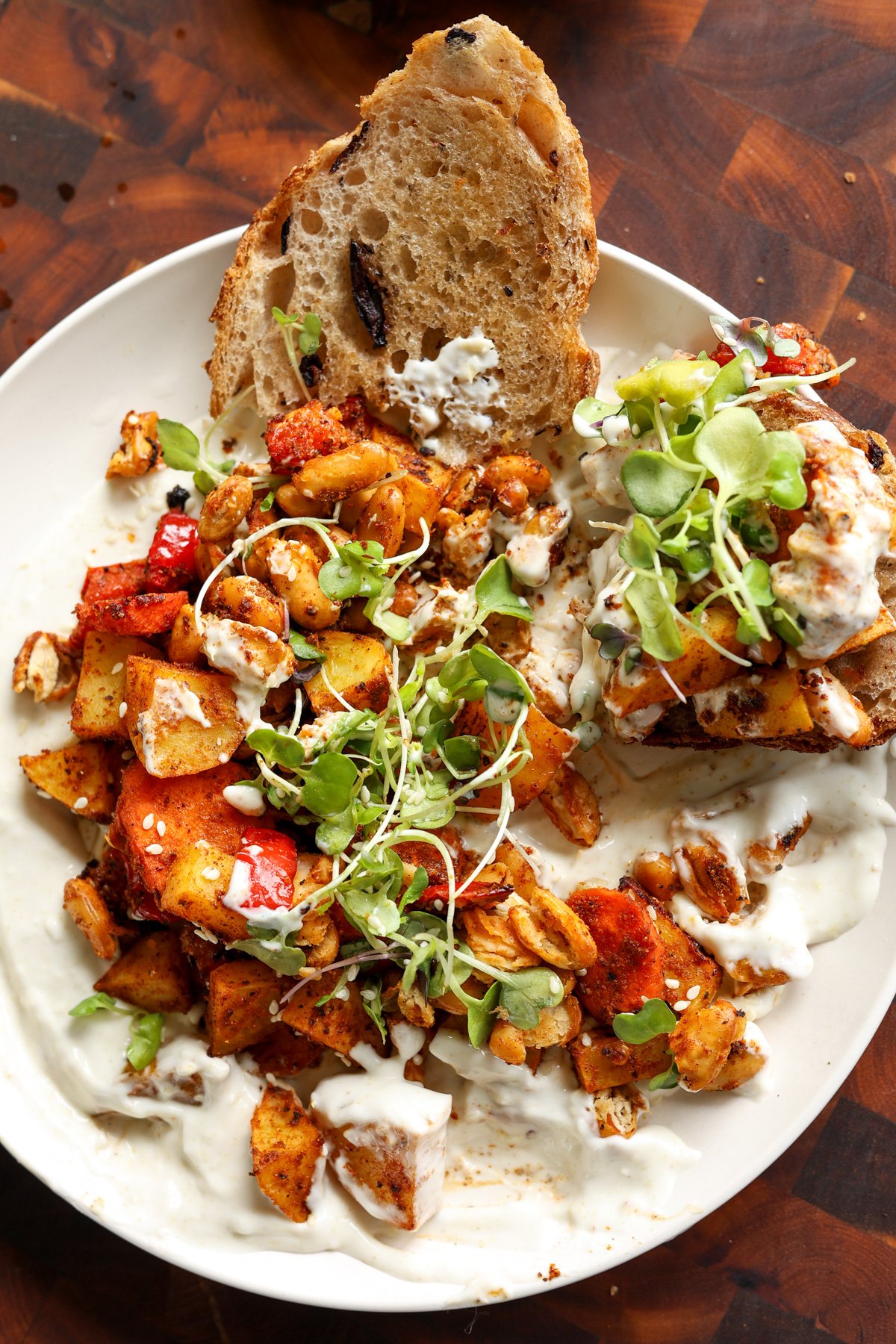 sheet pan veggies and beans over creamy lemon yogurt sauce on a white plate with bread for dipping