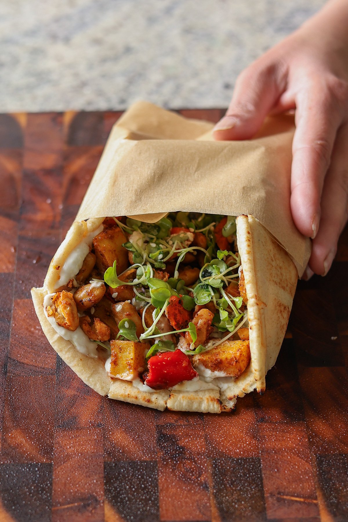 hand picking up a wrap made from making a wrap from sheet pan veggies and beans