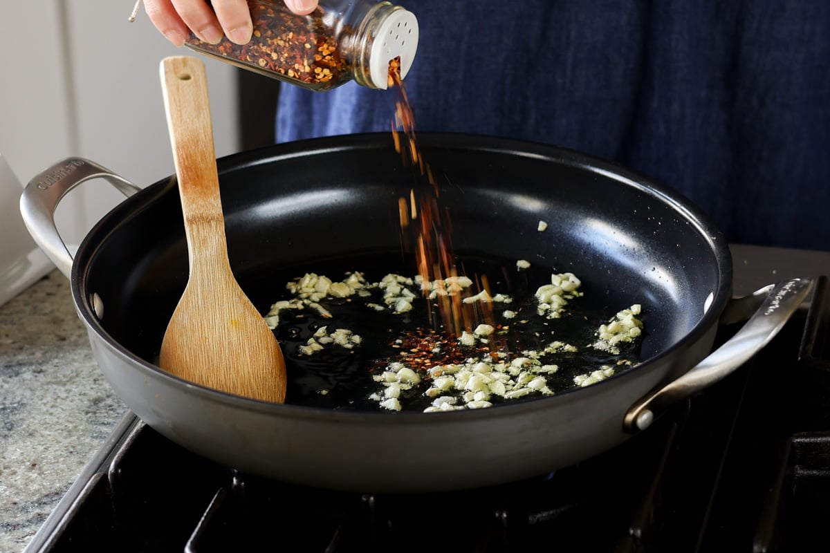 adding crushed pepper to the pan with the garlic