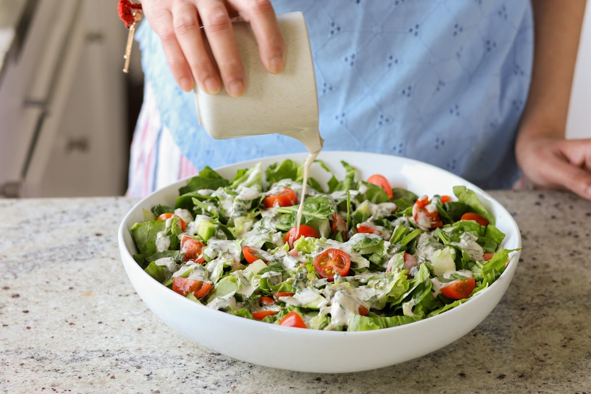 pouring the tahini dressing onto the spinach salad