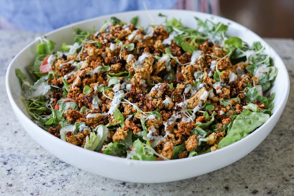 summer spinach salad with chickpea olive crumbles in a serving bowl
