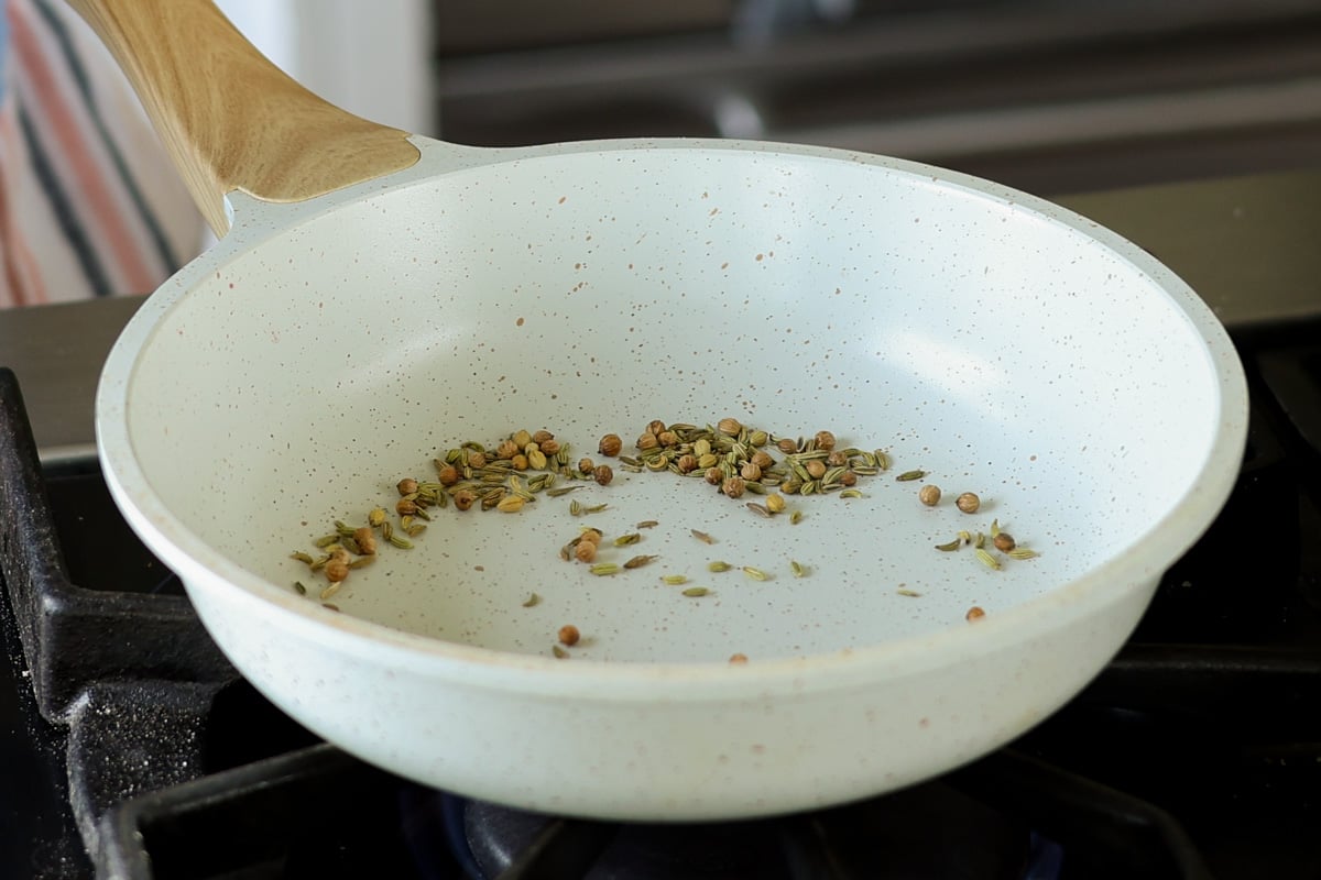 Fennel and coriander seed toasting in a white skillet.