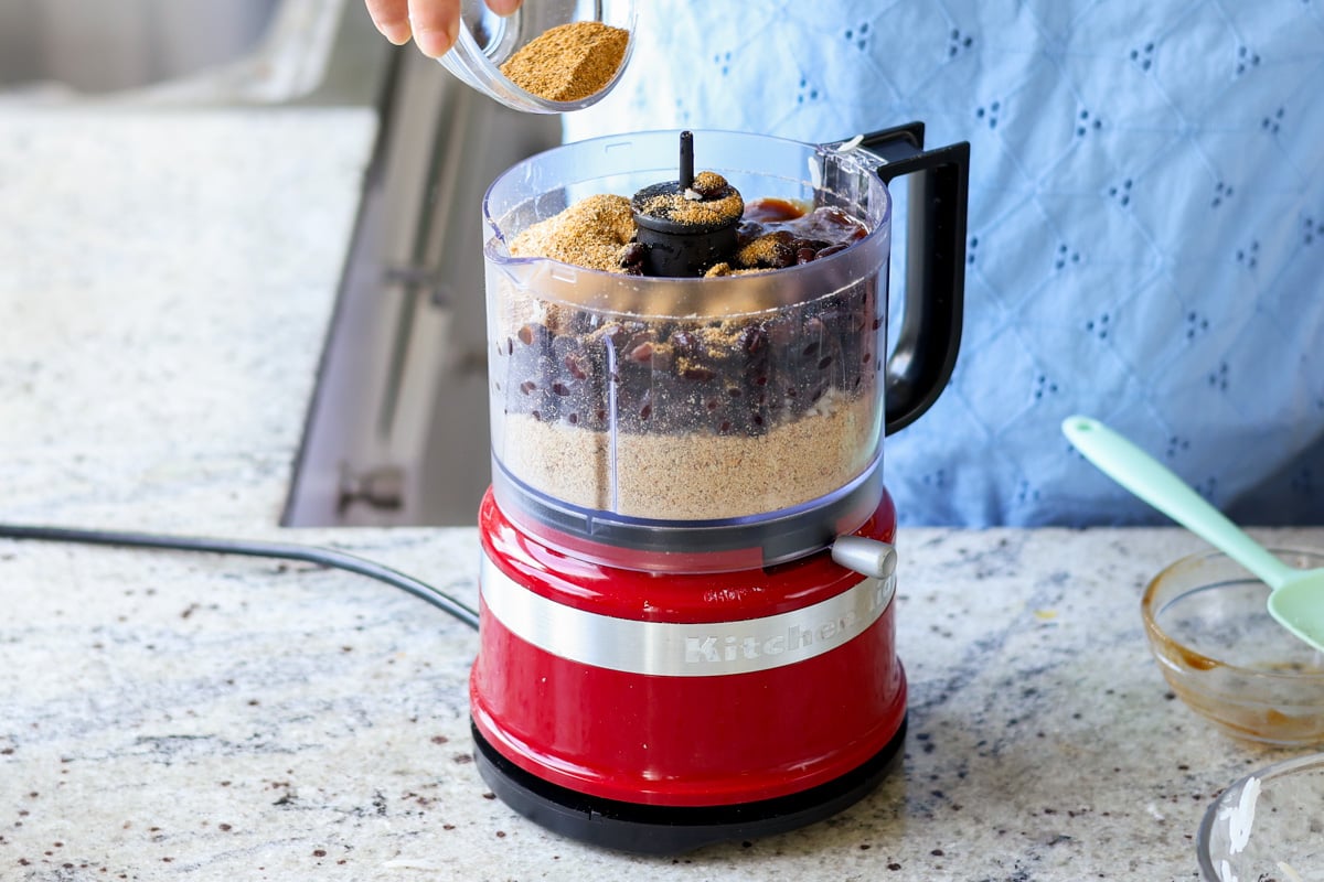Spices added to the food processor with black beans, ground seeds, and bbq sauce.