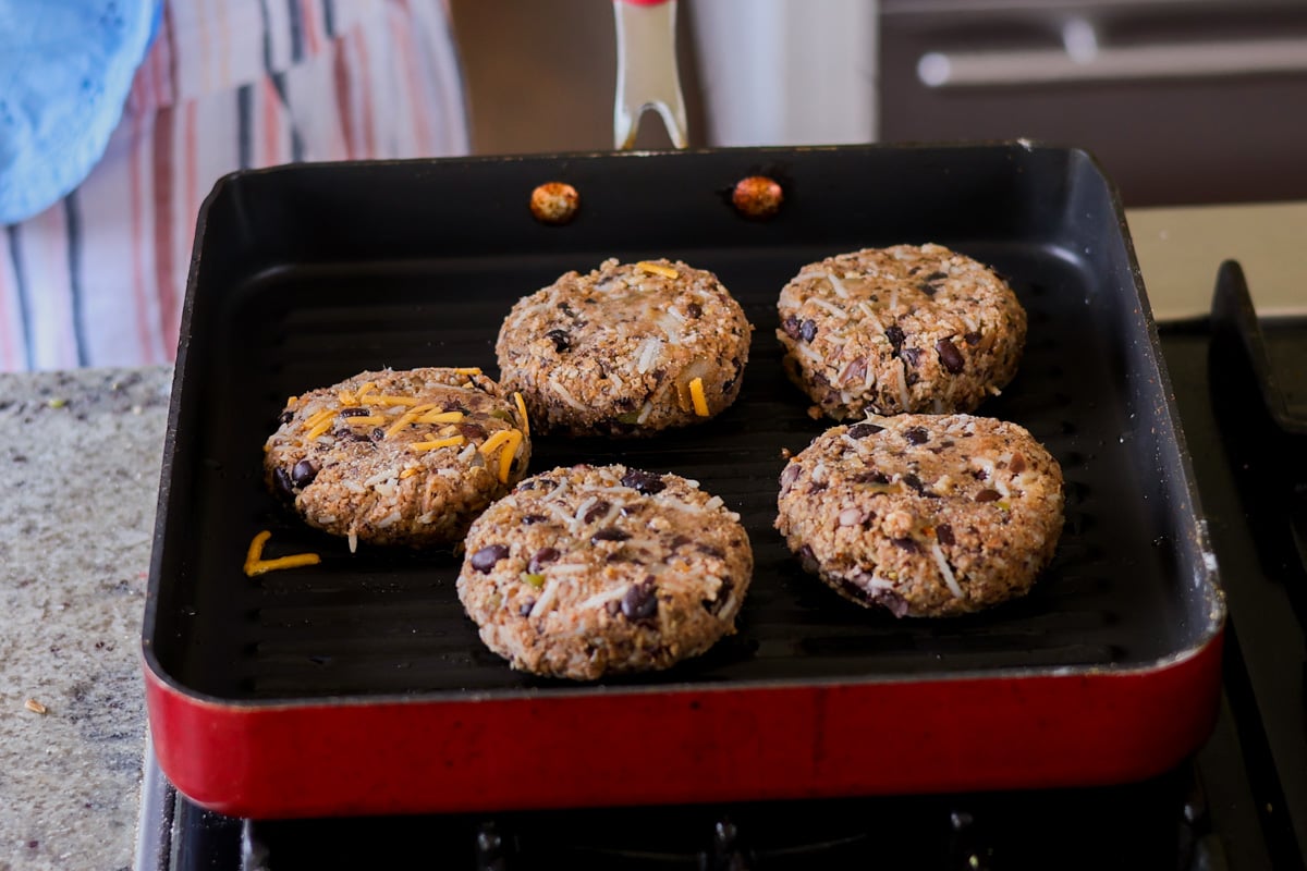 Five veggie burgers grilling in a red pan.