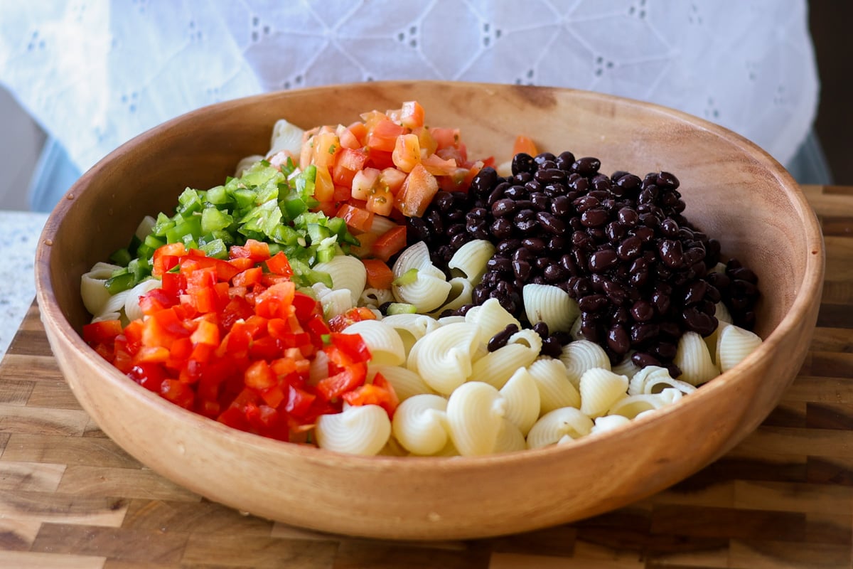 wooden bowl with black beans, pasta, red bell pepper, tomato, and green bell pepper.