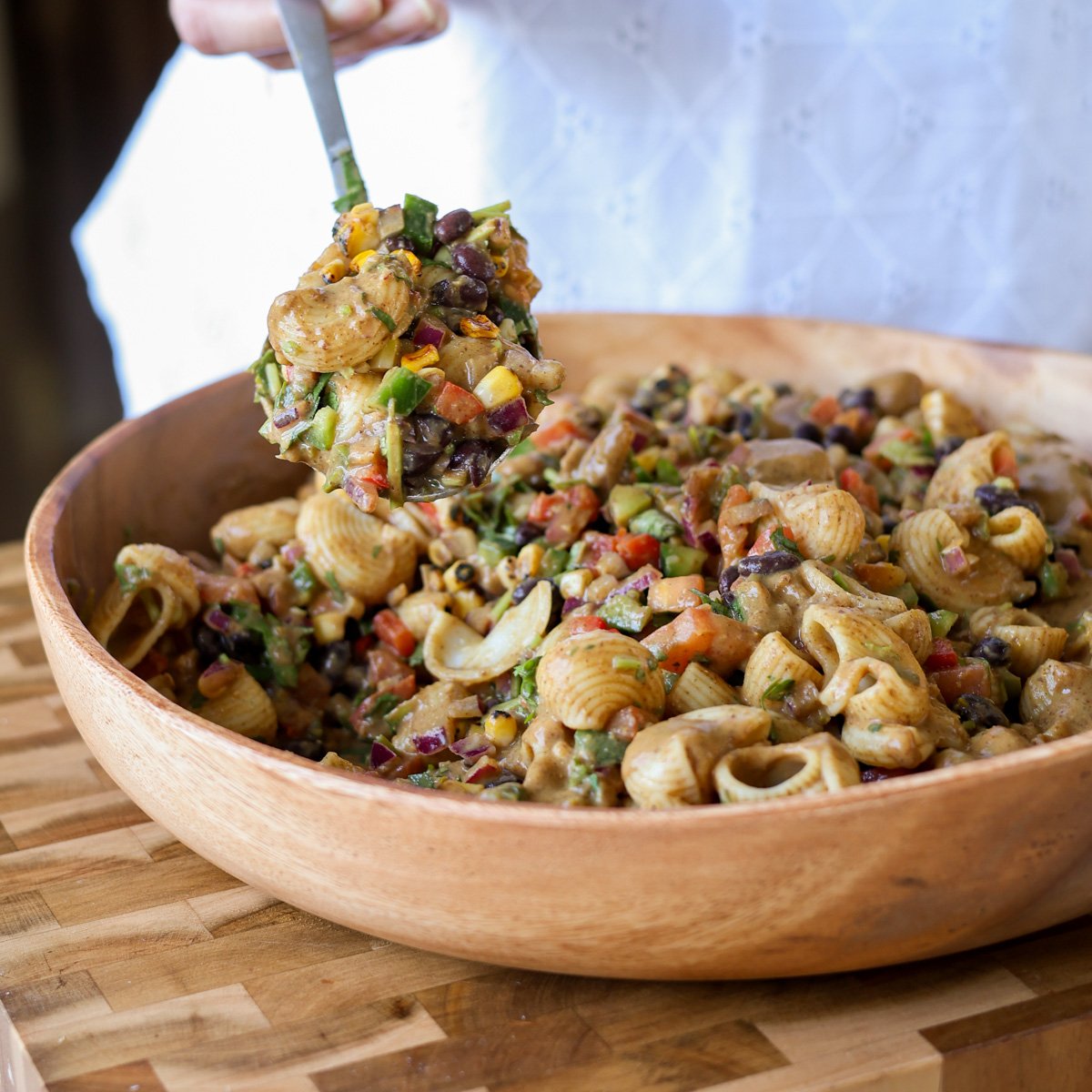 A large wooden bowl full of southwestern salad with a spoon scooping.