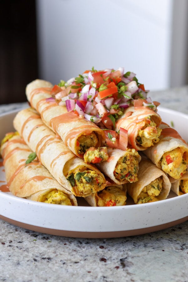 breakfast taquitos on a plate topped with pico de gallo and creamy hot sauce