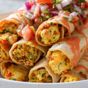 close up of breakfast taquitos on a plate topped with pico de gallo and creamy hot sauce