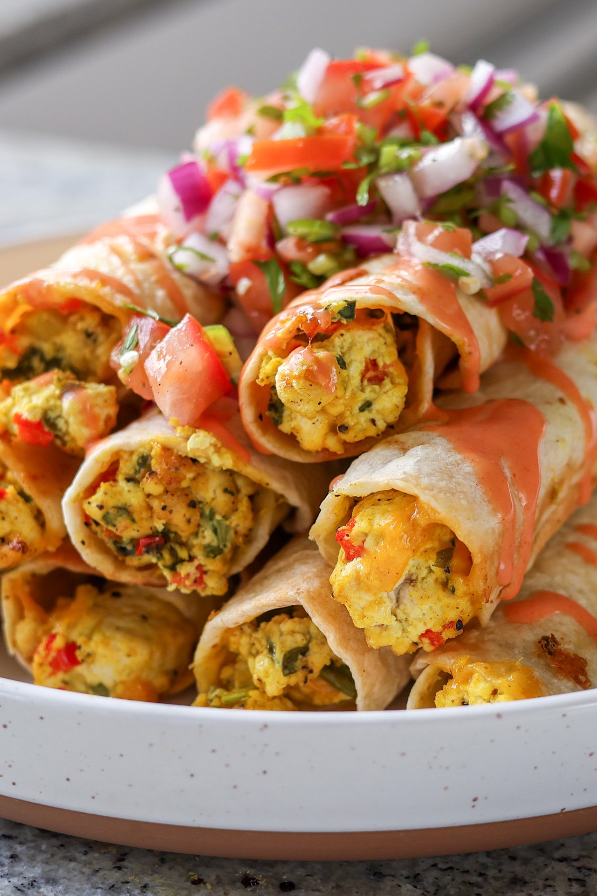 close up of breakfast taquitos on a plate topped with pico de gallo and creamy hot sauce