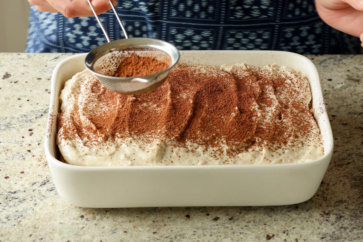 dusting the chai tiramisu cake with cocoa and cinnamon