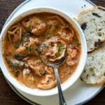 bowl of tortellini soup with a spoon and a side of bakery bread