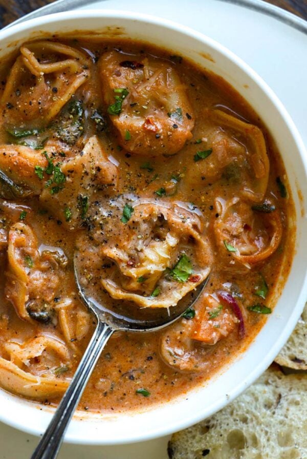 bowl of tortellini soup with a spoon and a side of bakery bread