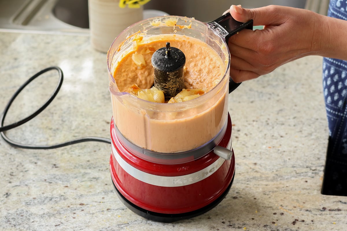 adding roasted garlic to the bean puree in the food processor