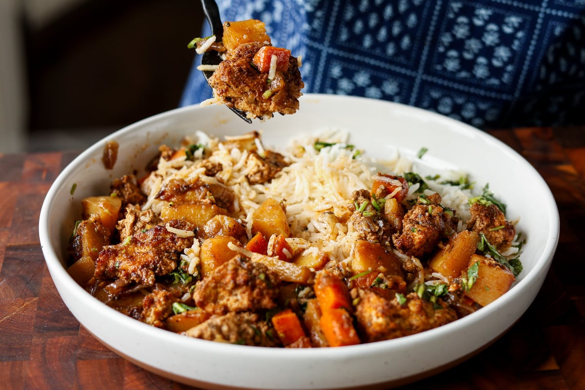 fork taking a bite of braised tofu and veggies with rice and herb sauce