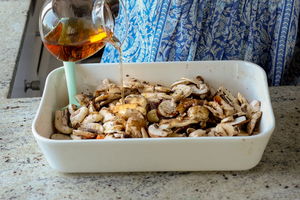 adding mushrooms and stock to the baking pan