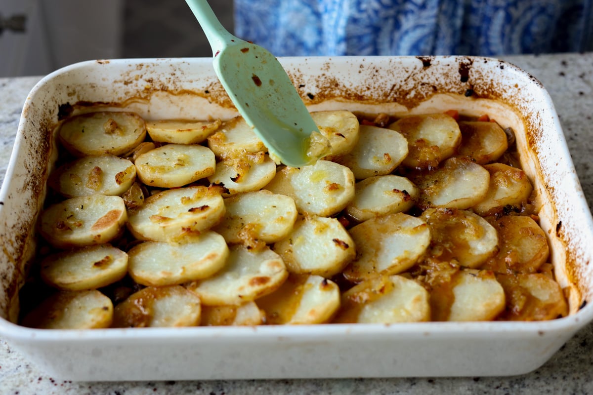spreading extra garlic butter onto baked mushroom potato casserole