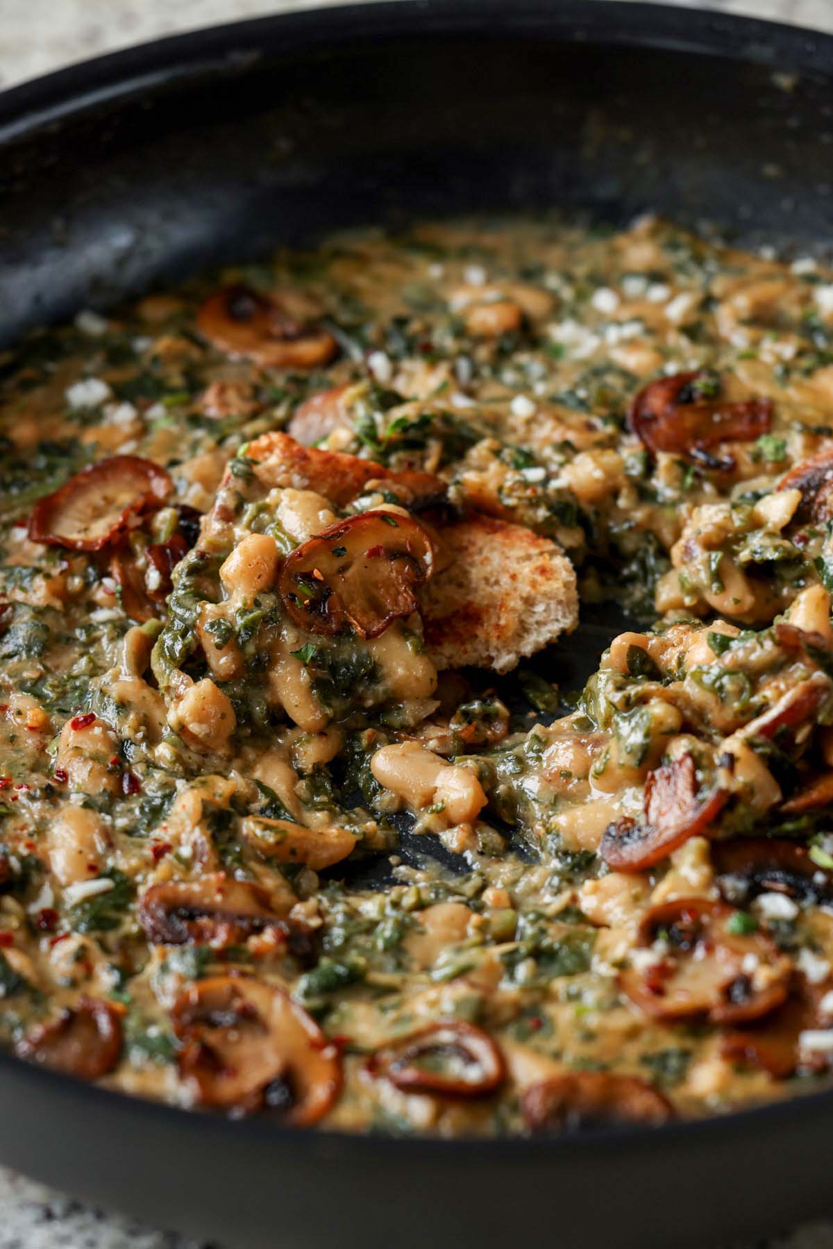close-up of dipping bread into the spinach mushroom beans