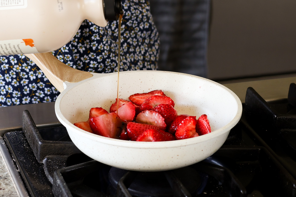 adding strawberries and maple syrup to a pan