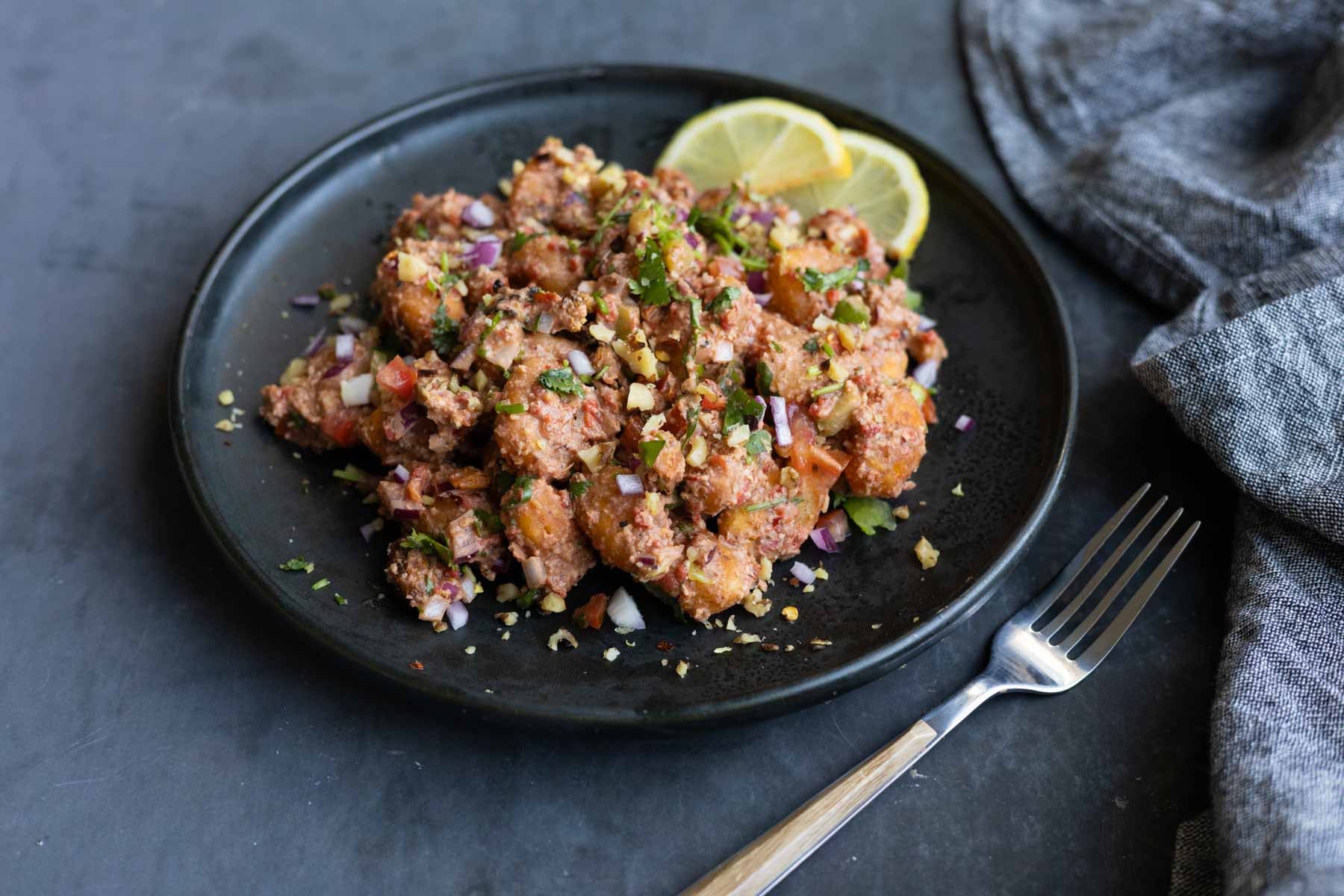 crispy gnocchi muhammara salad on a plate with lemon slices
