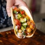 hand holding a wrap with peri-peri chickpeas topped with the salsa and other garnishes