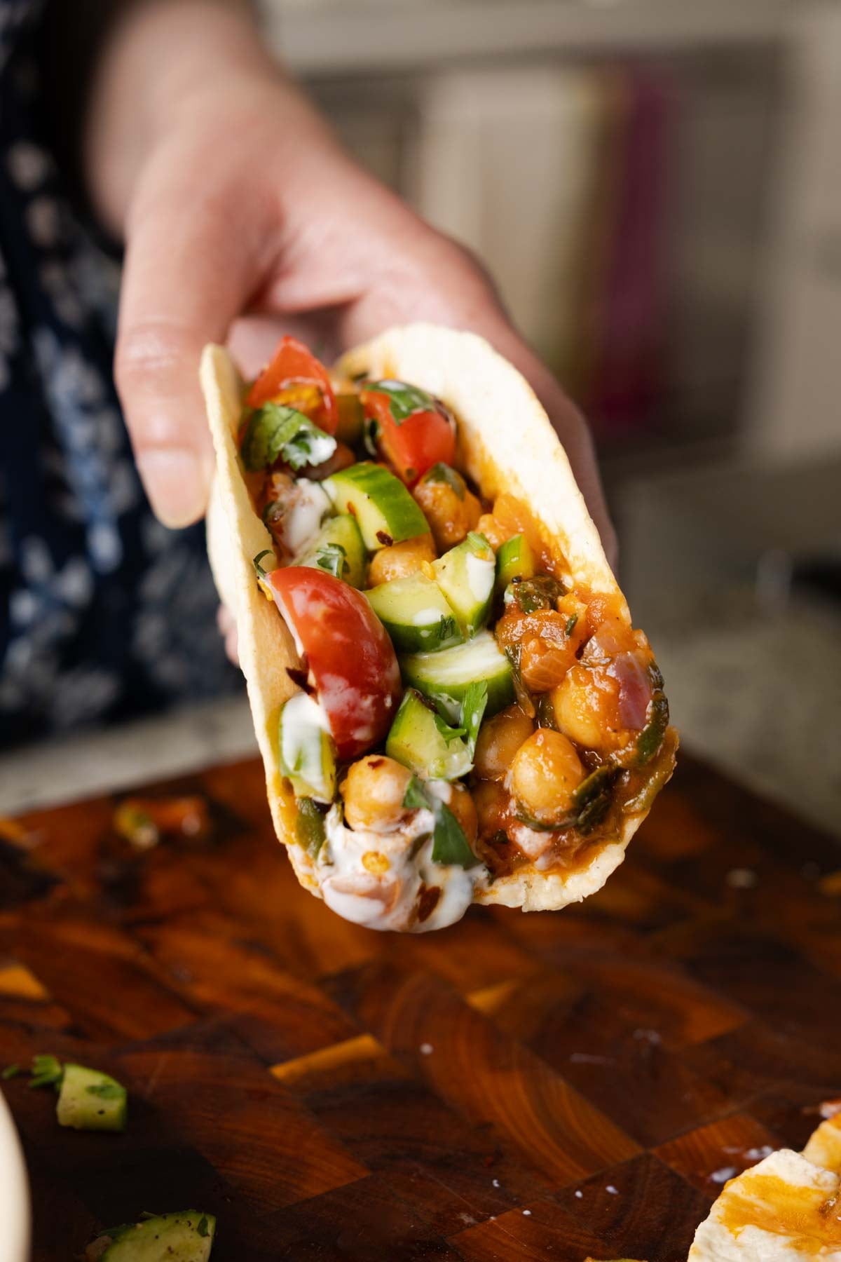 hand holding a wrap with peri-peri chickpeas topped with the salsa and other garnishes