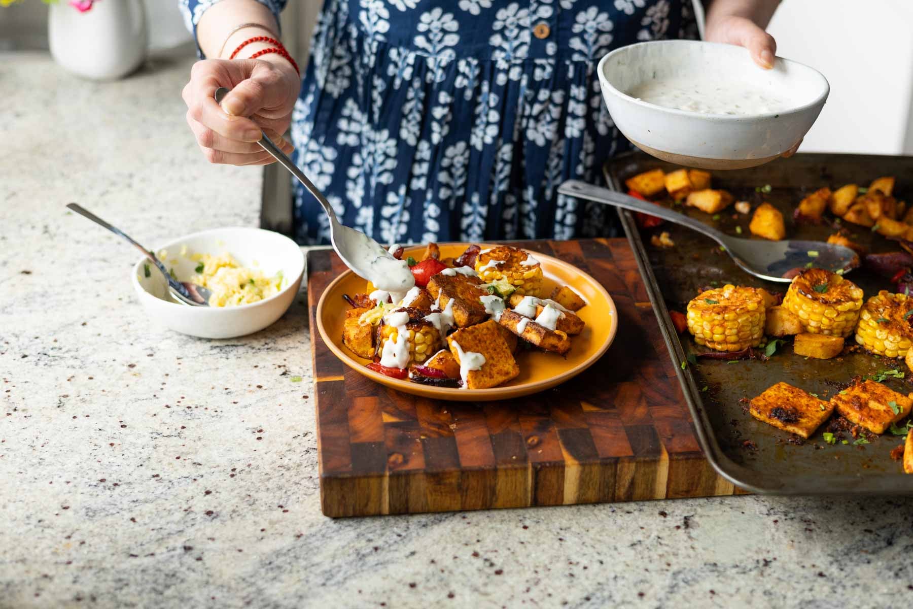 adding yogurt sauce to the peri-peri tofu and vegetables on a plate