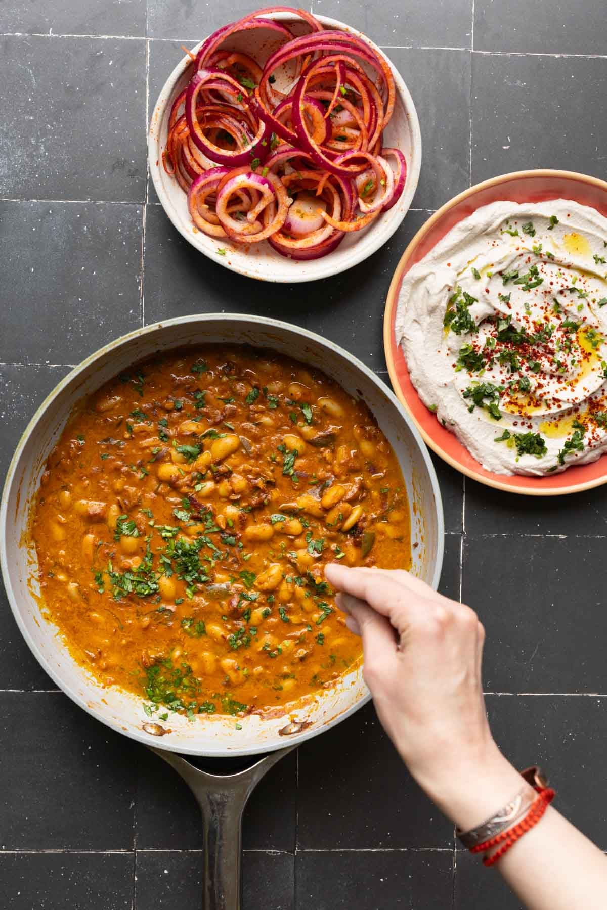chili garlic beans, onion salad, and whipped tofu in bowls on a black table